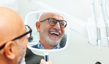 Man with glasses smiling at reflection in handheld mirror