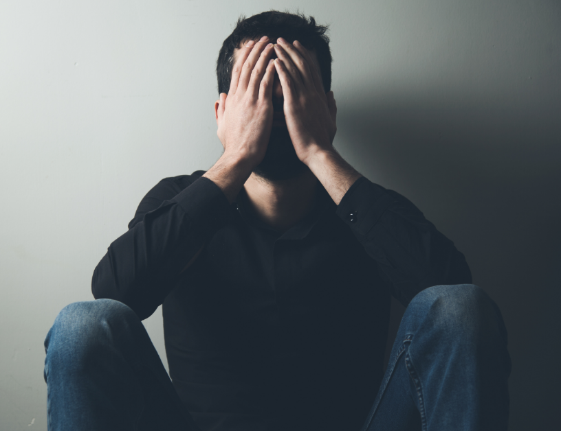 Man sitting against wall, head in hands