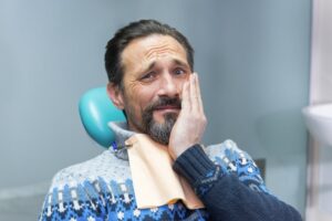 Man in dentist’s chair holding mouth in pain.